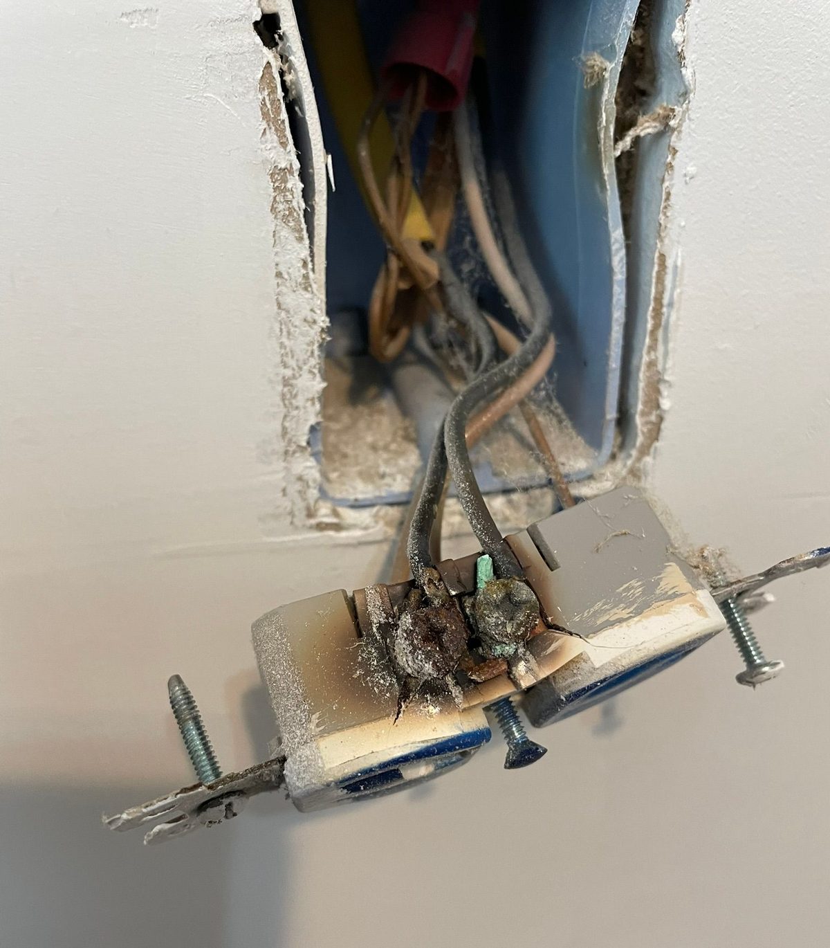 Burnt electrical outlet with exposed wires and scorched surrounding wall.