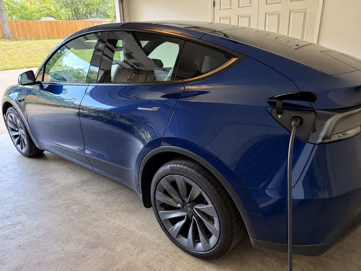 Tesla charging in an open garage with the connector plugged into the rear charge port.