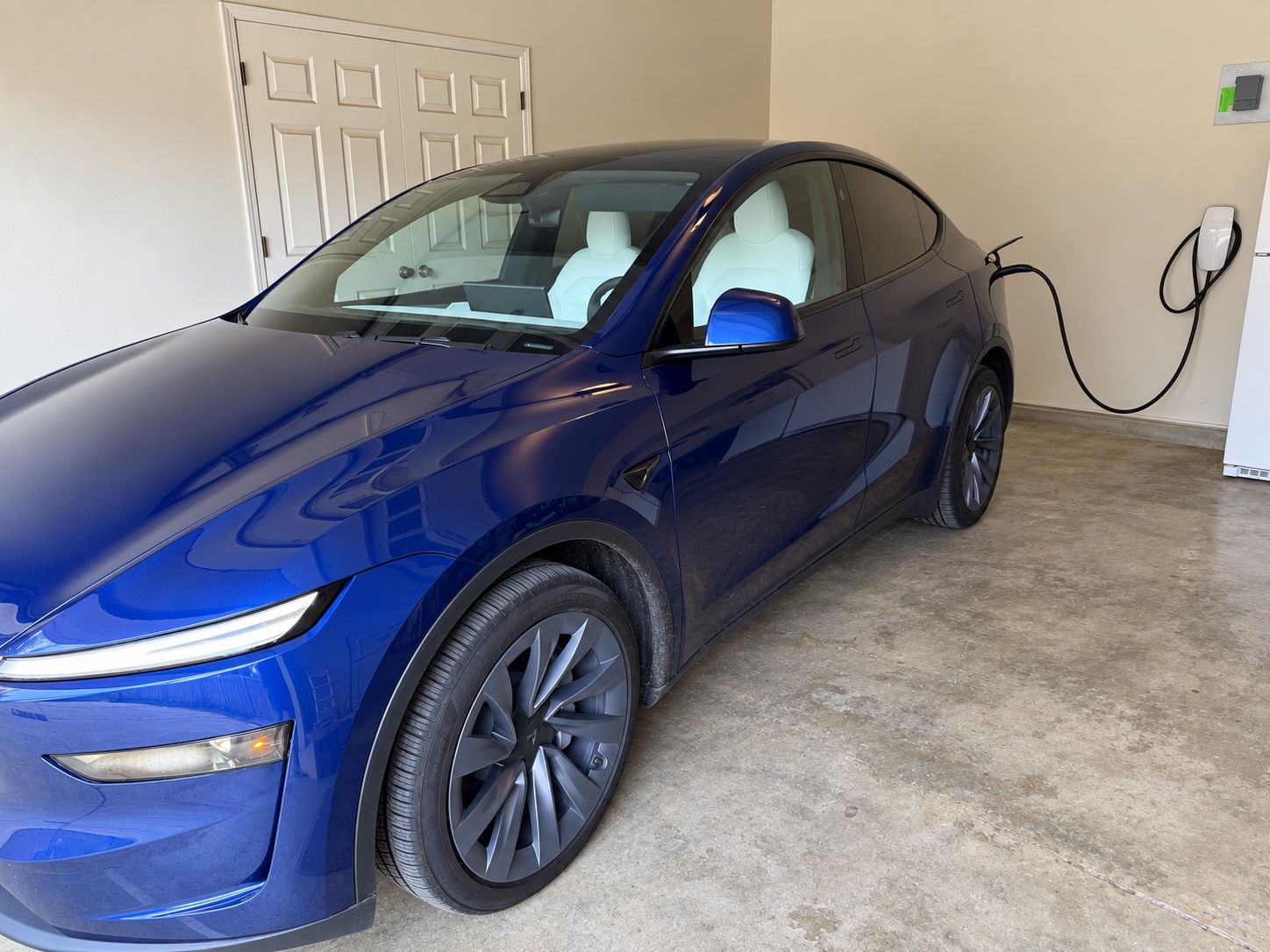 Tesla parked in a garage beside a wall-mounted charger with the cable running to the car.